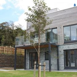 Modern two-story house with stone and wood exterior, large windows, and a glass balcony.