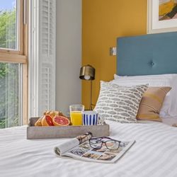 Breakfast tray with fruit, juice, and coffee on a bed near a window in a cozy bedroom.