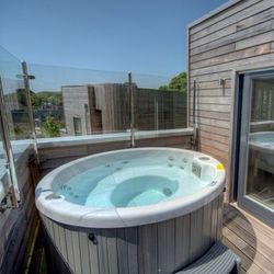 Outdoor hot tub on a wooden balcony next to a bedroom with large glass doors