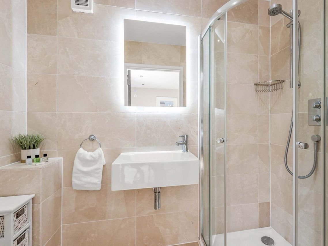 Modern bathroom with glass shower enclosure, sink, towel, and backlit mirror