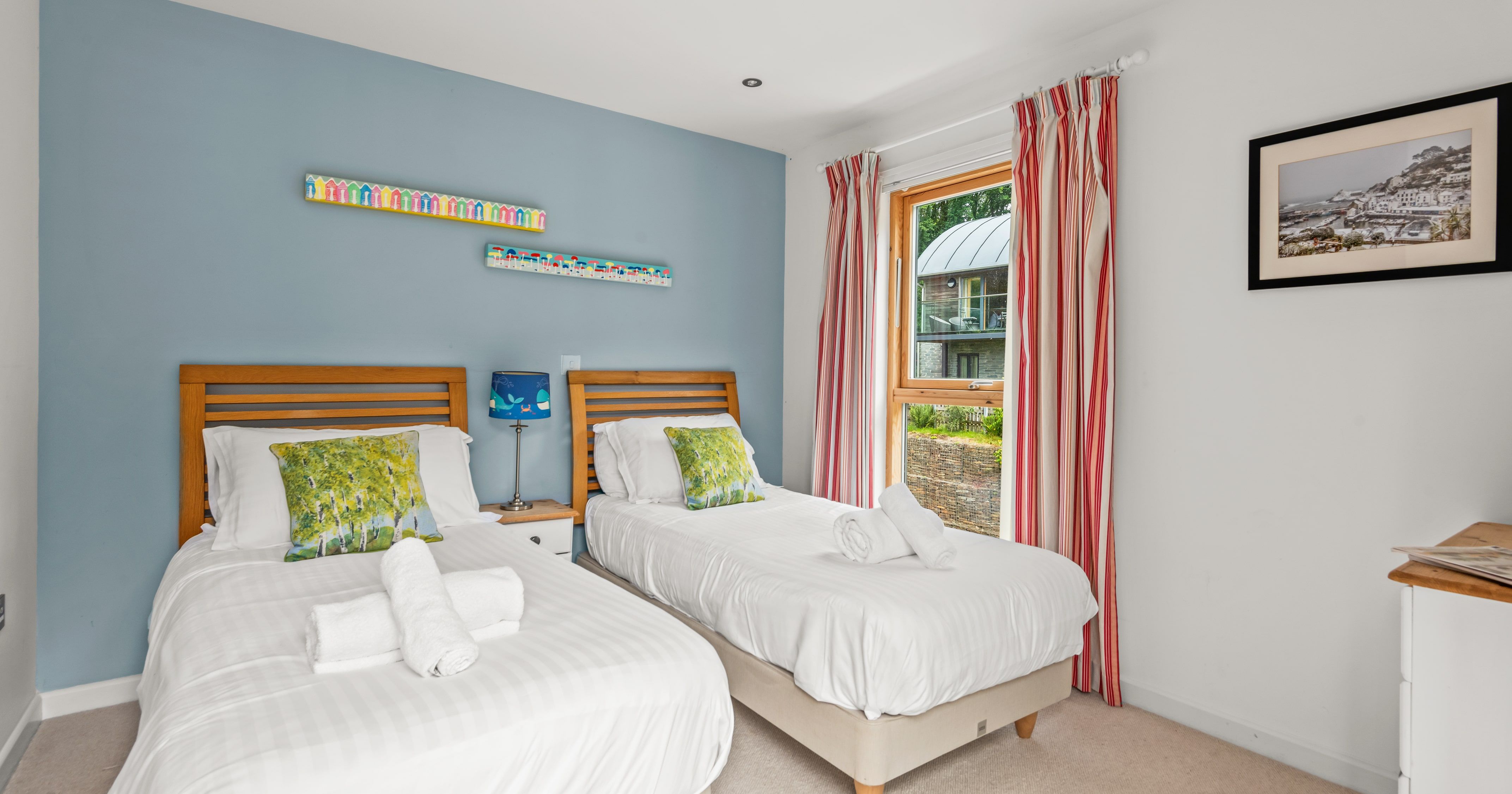Cozy twin bedroom with two single beds, colorful pillows, and a large window with striped curtains.