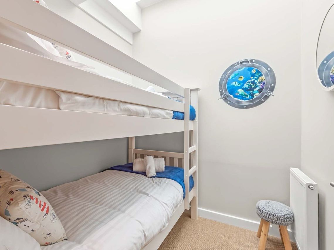 Bright and tidy children's room with white bunk beds, a round window showing an underwater scene, and a small stool.