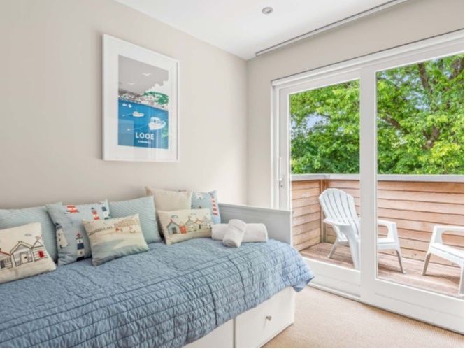 Cozy bedroom with a blue daybed, decorative pillows, and access to a balcony with outdoor chairs