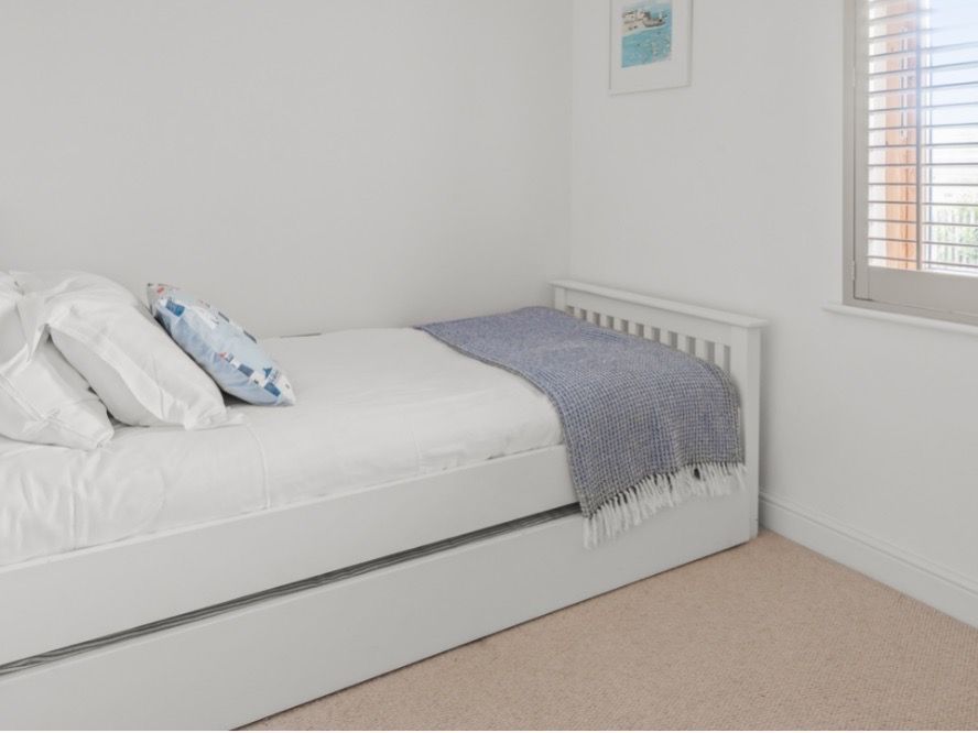 Minimalist bedroom with a single white bed, pillows, a blue throw, and a window with shutters.