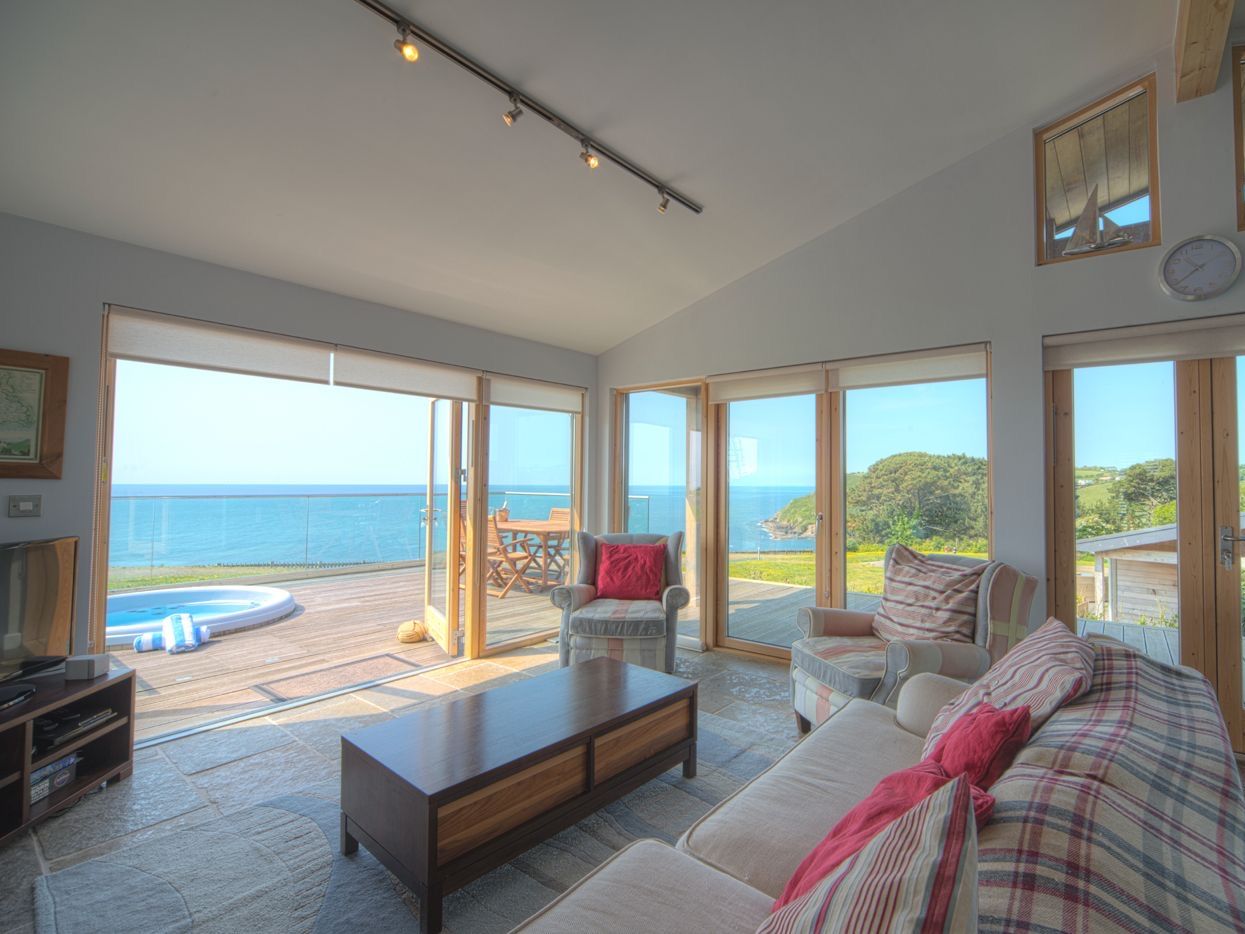 Modern living room with large windows overlooking the ocean and a deck with a hot tub and outdoor seating