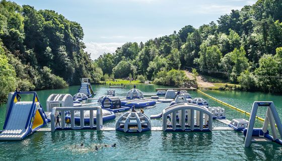 Large inflatable water park obstacle course on a lake surrounded by trees.