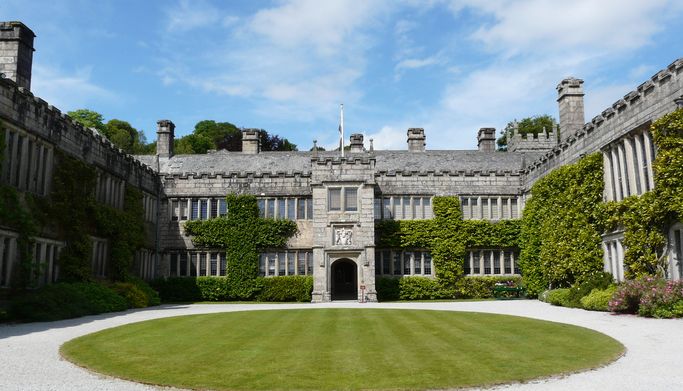 Historic stone manor house with ivy-covered walls and a large circular lawn in the courtyard.
