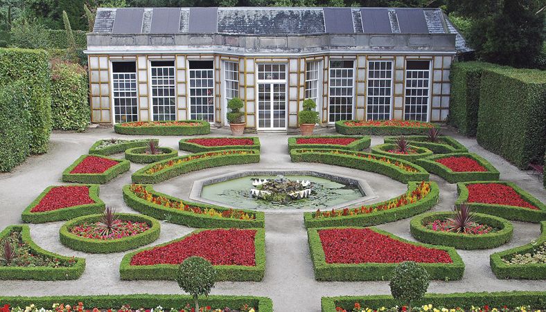 Formal French garden with geometric flower beds and a central pond in front of a classical building.