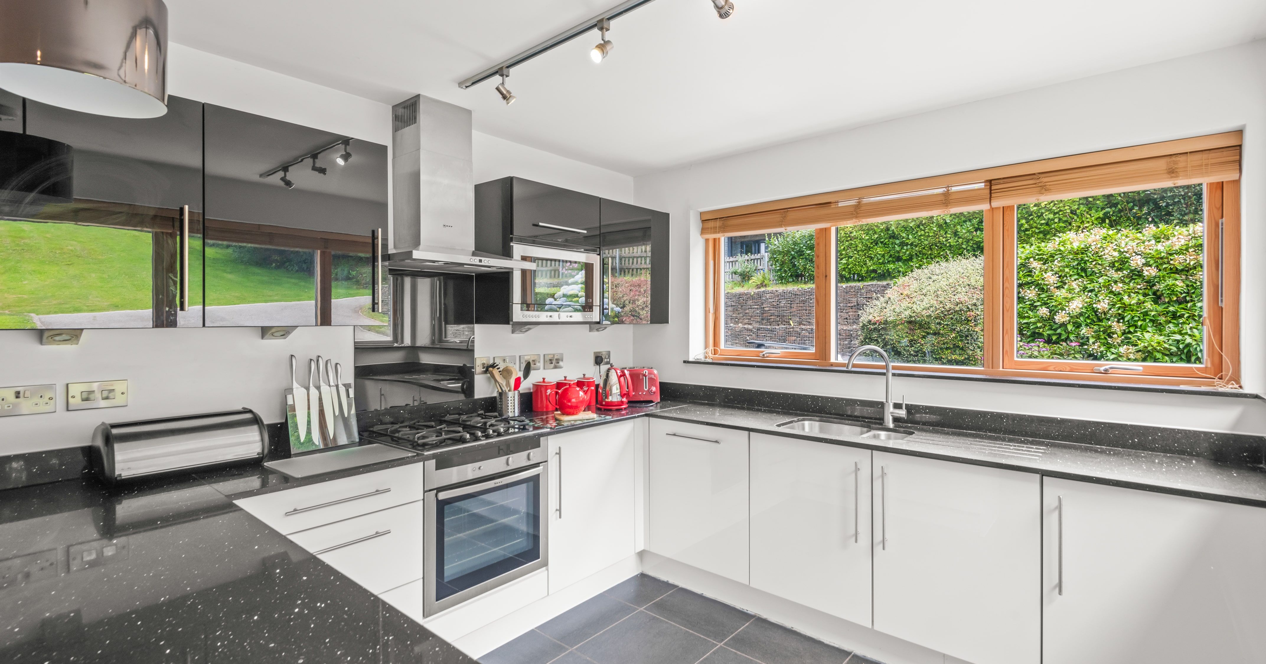 Modern kitchen with white cabinets, black countertops, stainless steel appliances, and large windows overlooking a green garden.