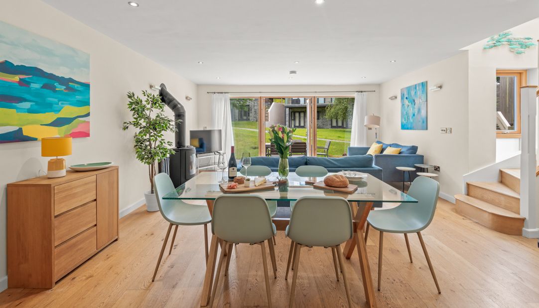 Open-plan living and dining area with glass table, pastel chairs and blue sofa looking out to a garden