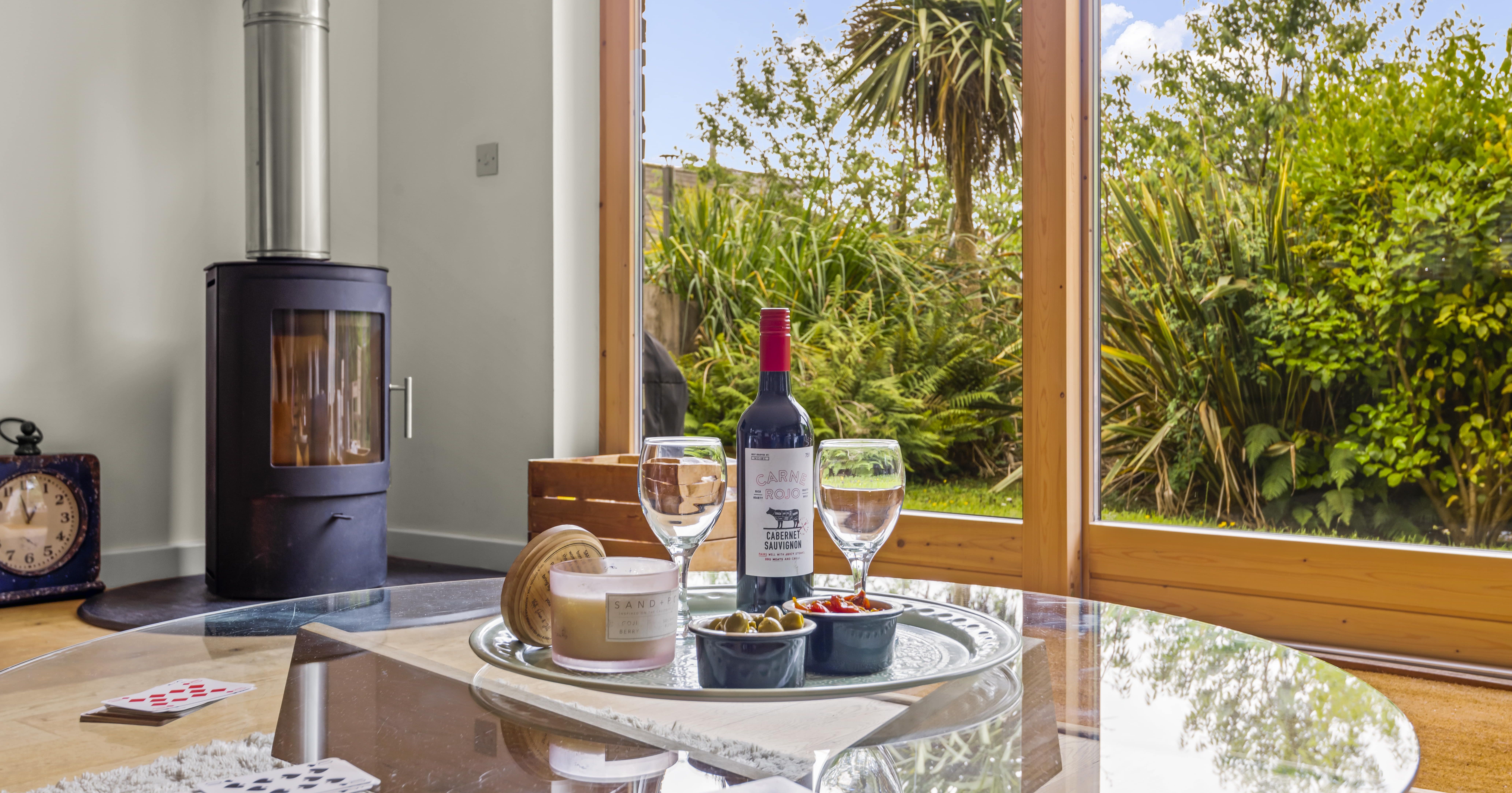 Wine and glasses on a table in front of a window with garden view and a wood-burning stove