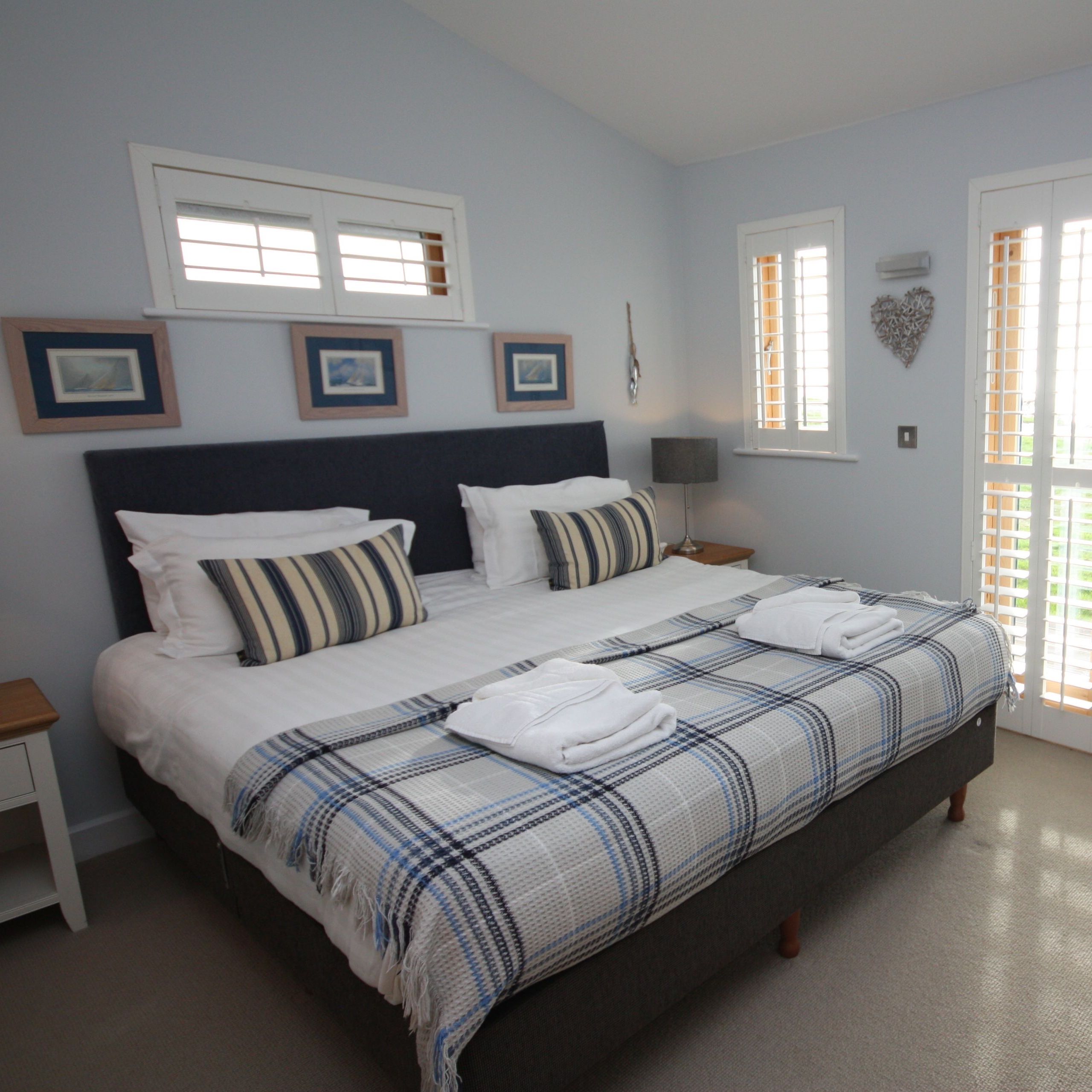 Bright double bedroom with plaid throw, striped cushions and shuttered French doors