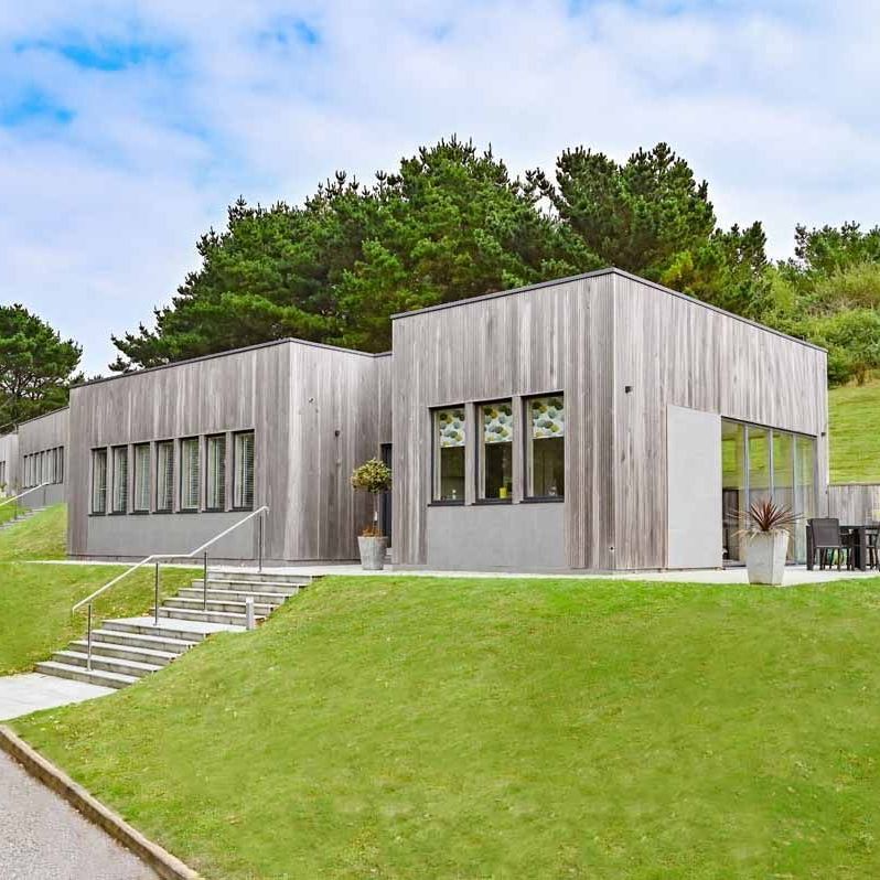 Modern timber-clad building on a grassy slope beside a paved path and steps
