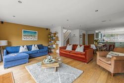 Modern open-plan living room with blue and orange sofas, wooden floors, and a kitchen in the background.