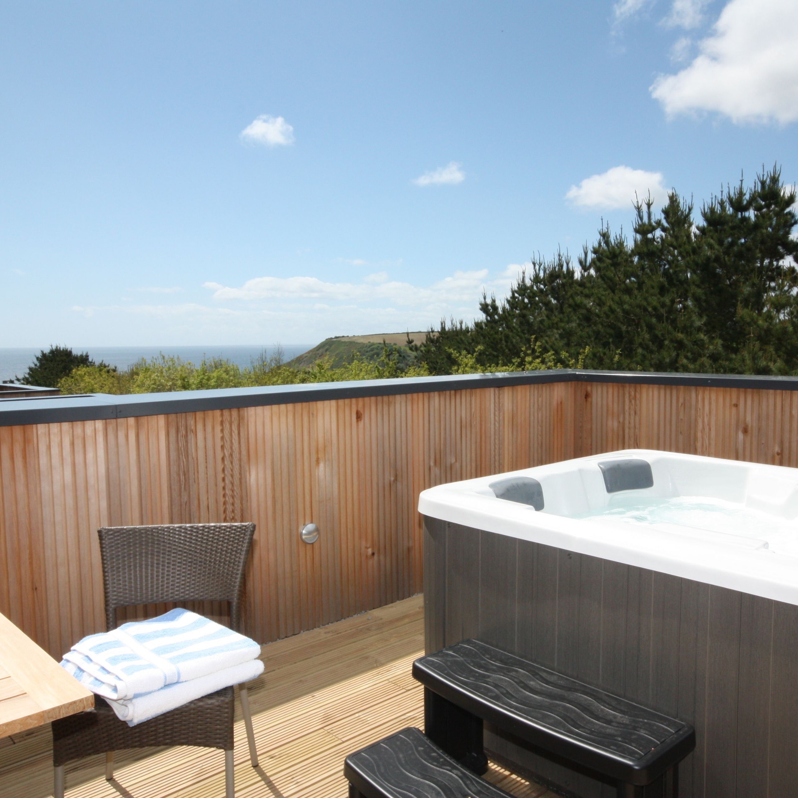 Outdoor hot tub on a wooden deck with champagne and sea view under blue sky