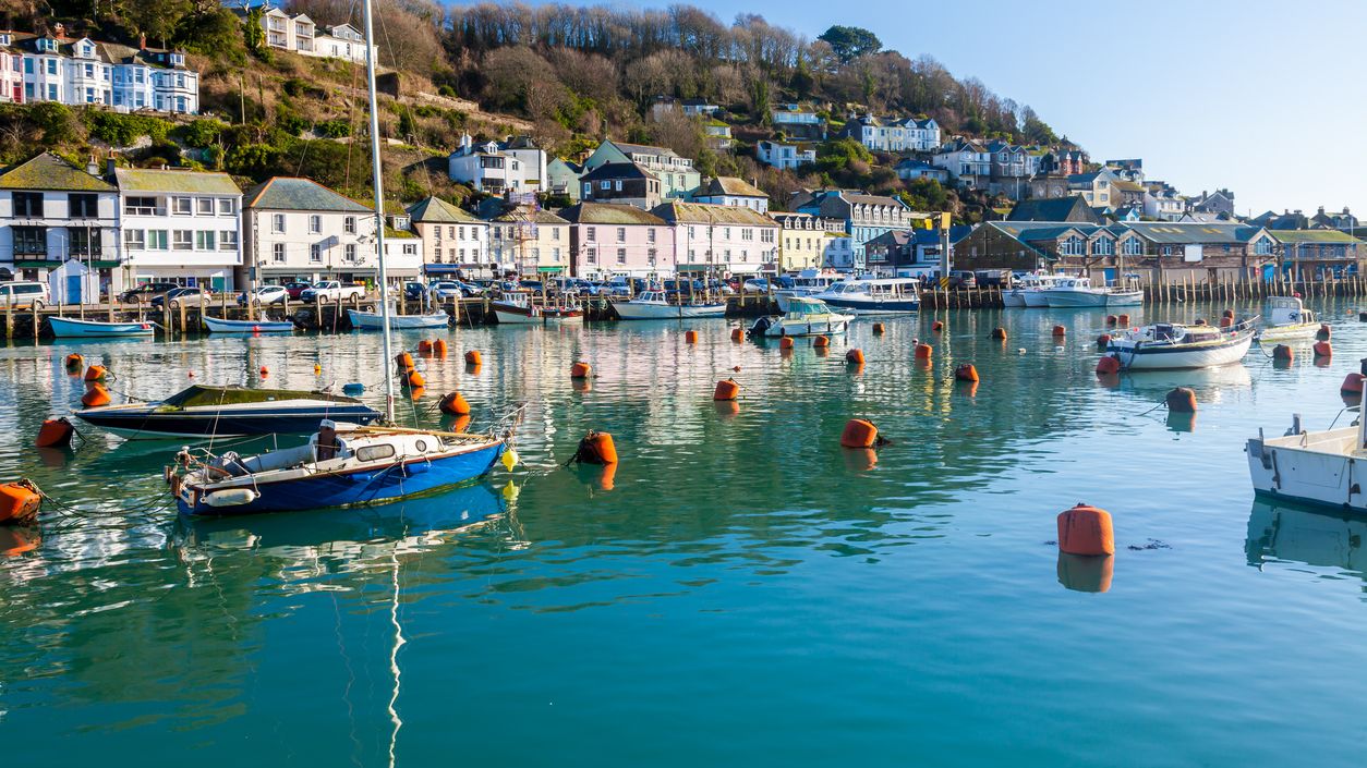 Harbour with moored boats and orange buoys in calm water, with hillside houses under a clear blue sky