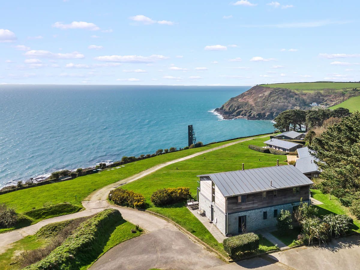 Aerial view of modern coastal buildings on a grassy headland overlooking the sea and cliffs