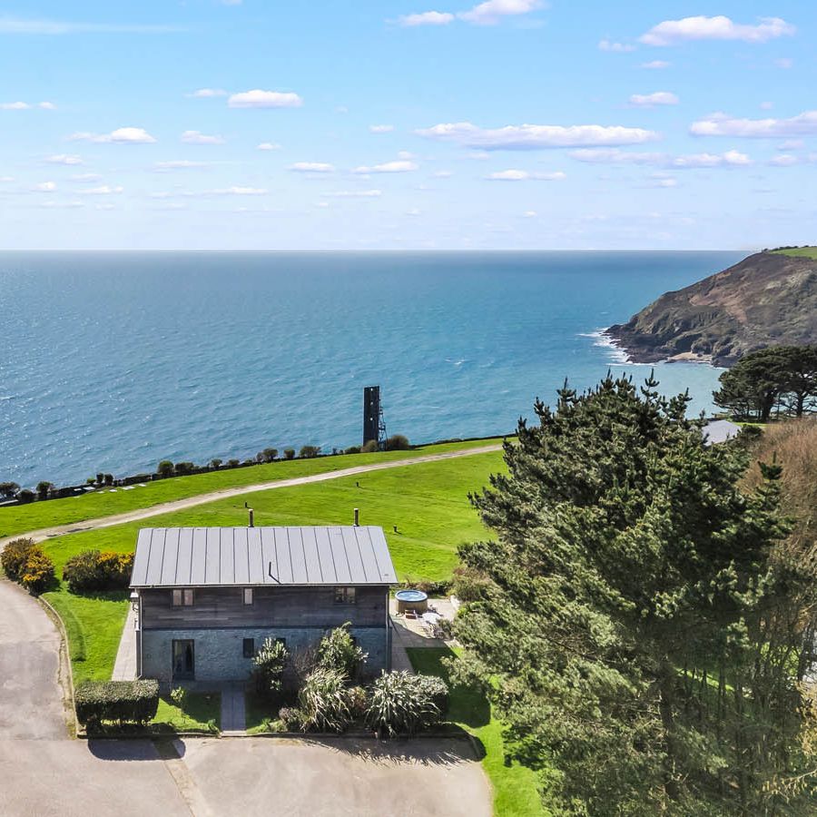 Aerial view of a coastal house with green lawns, winding drive and sea beyond under a blue sky