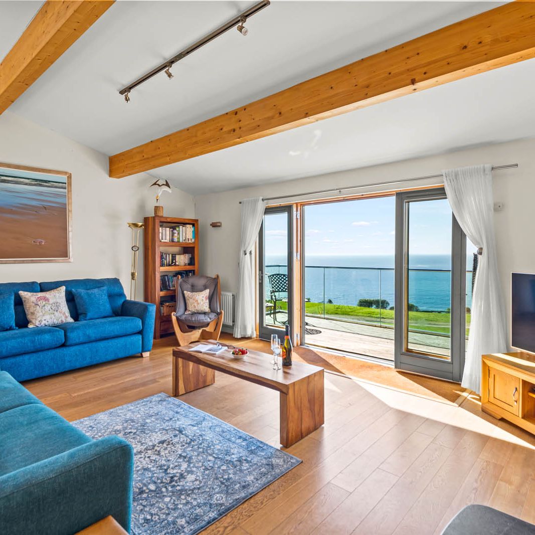 Bright coastal living room with blue sofas and floor-to-ceiling patio doors opening to a sea-view balcony