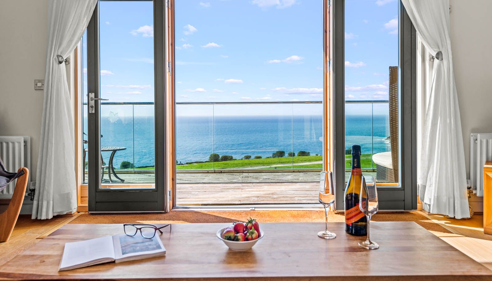 Ocean view through large patio doors with white curtains, table set with champagne, glasses and strawberries