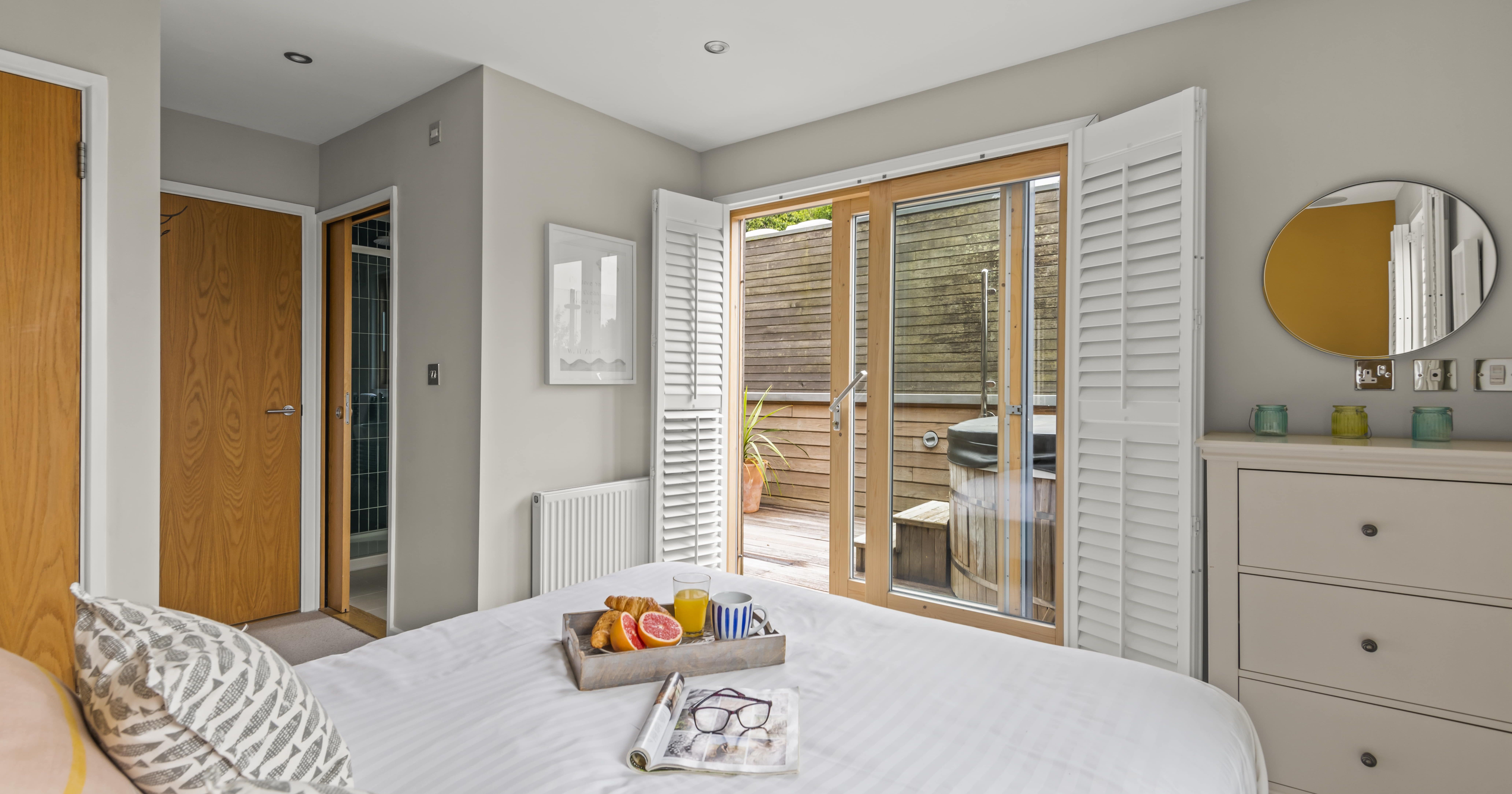 Bright bedroom with bed, tray of breakfast, and glass doors opening to patio with hot tub