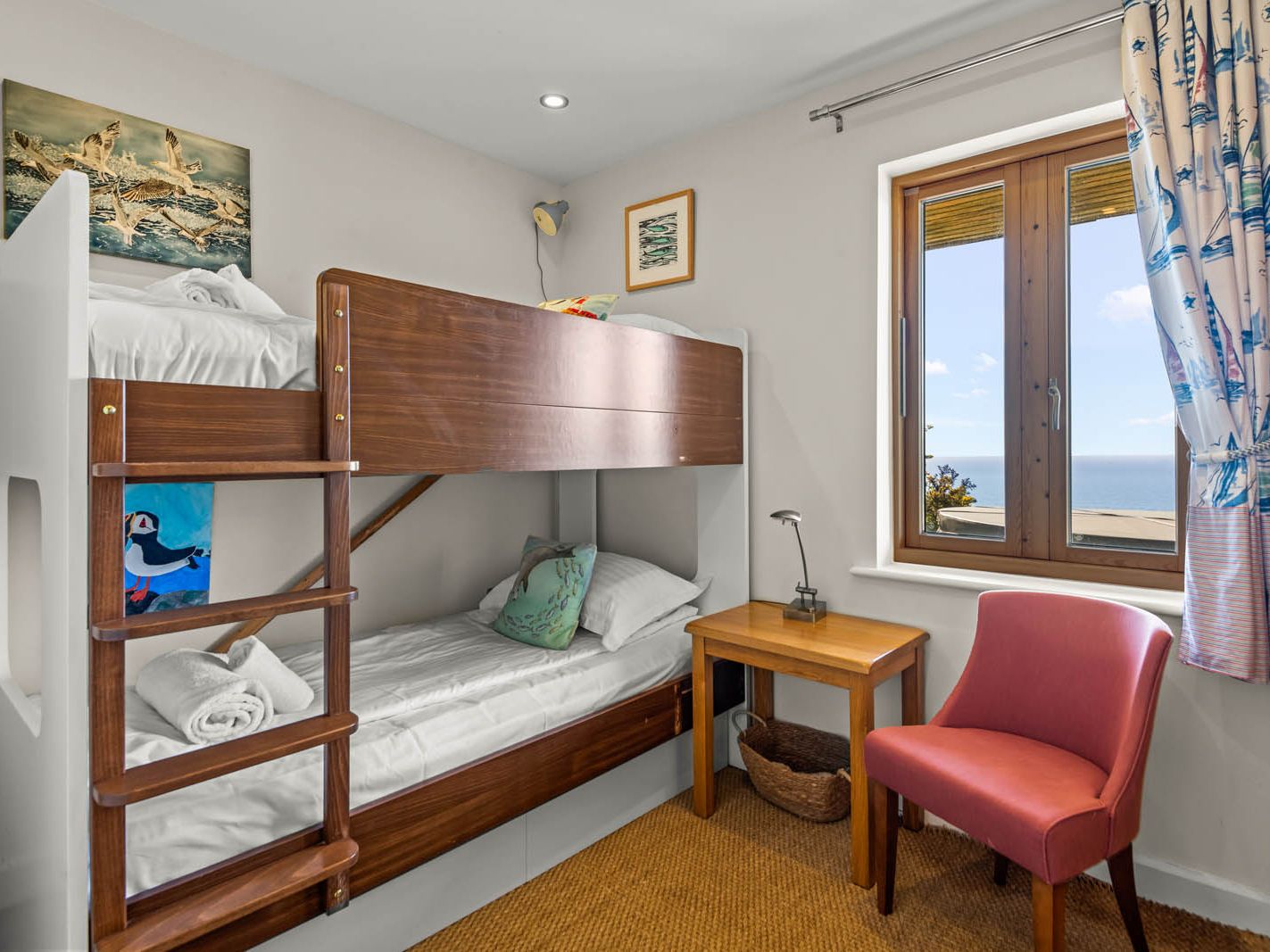 Bunk bed in a bright coastal bedroom with a desk by the window
