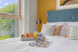 Breakfast tray with croissant, grapefruit, orange juice and coffee on a bed with decorative pillows, beside a window with a garden view