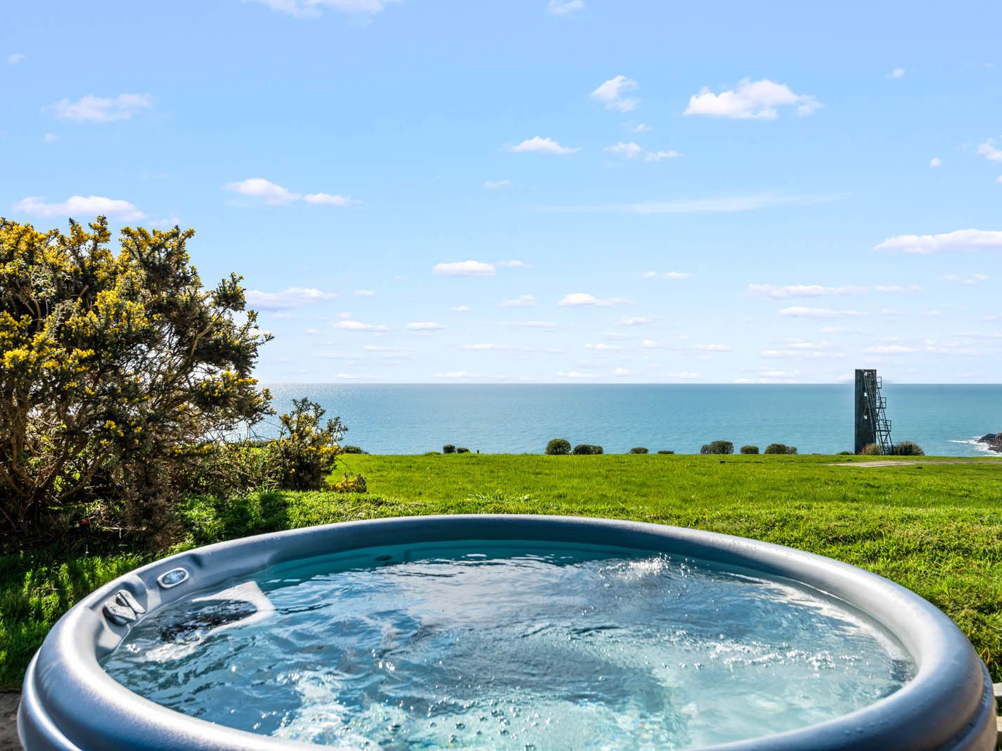 Hot tub overlooking a grassy clifftop and the sea under a blue sky
