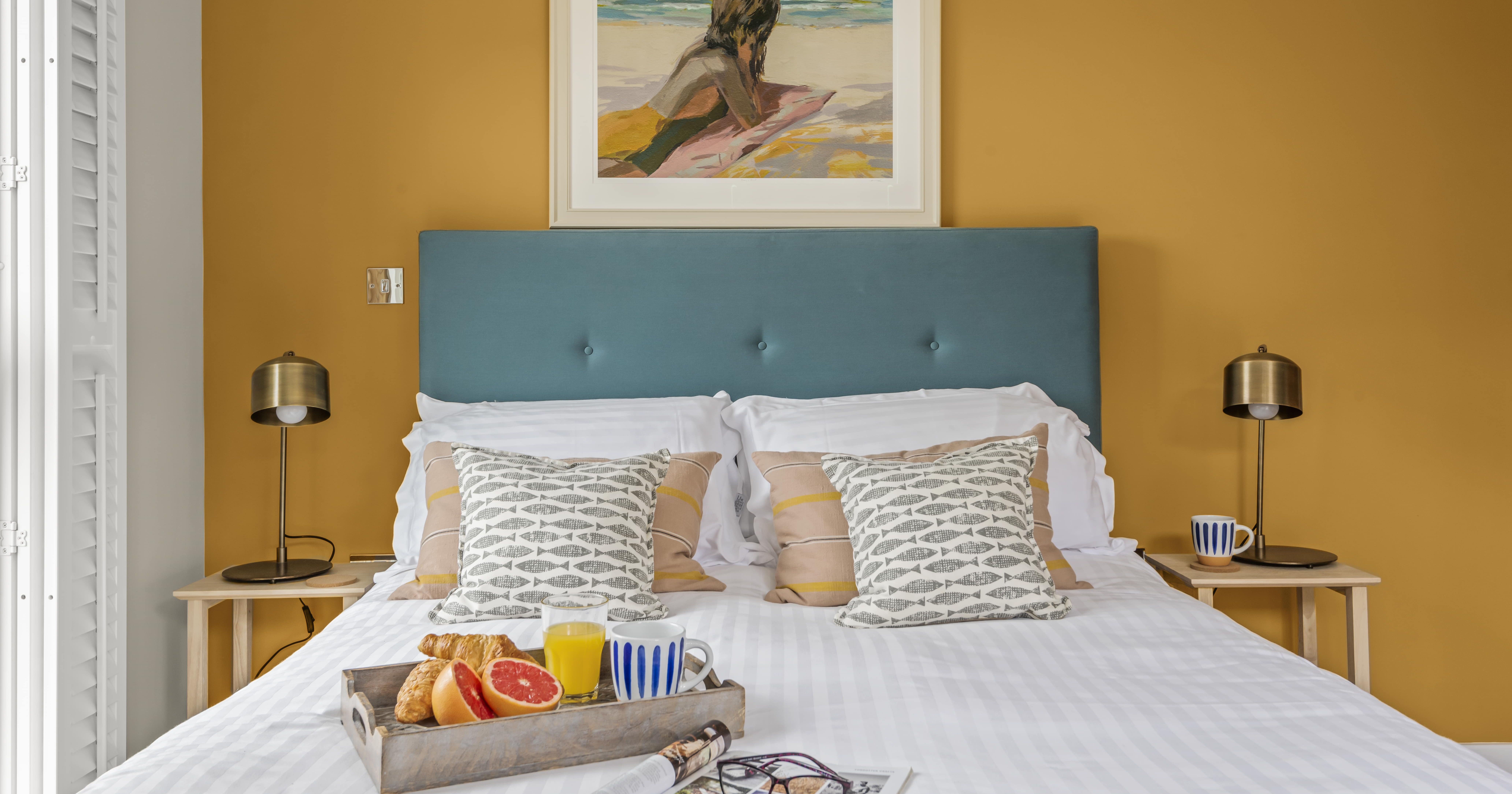 Cozy modern bedroom with mustard yellow walls, blue headboard, and breakfast tray on bed