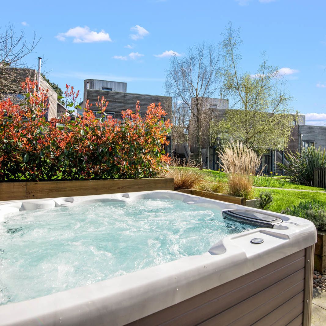 Outdoor hot tub on a patio beside landscaped garden with modern buildings in the background