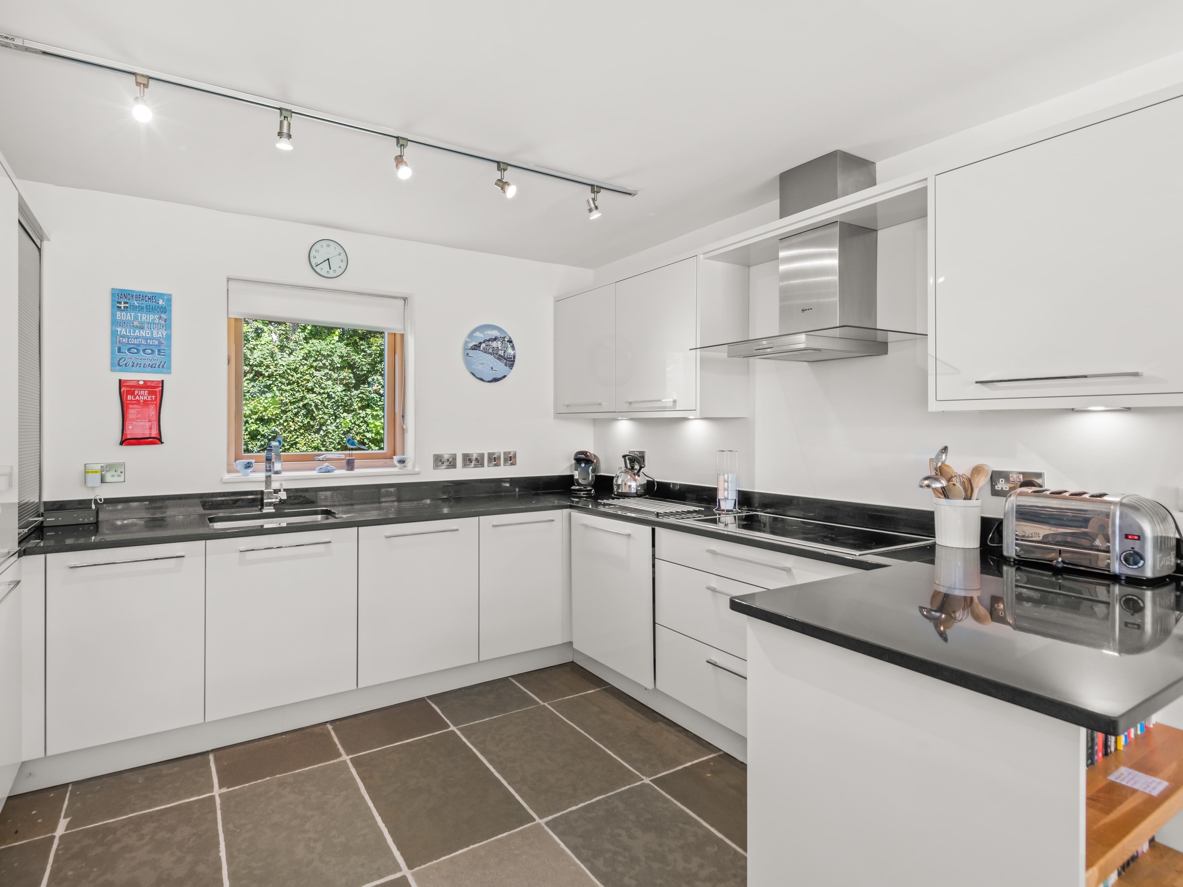 Modern white kitchen with black worktops, built-in oven, and window above the sink