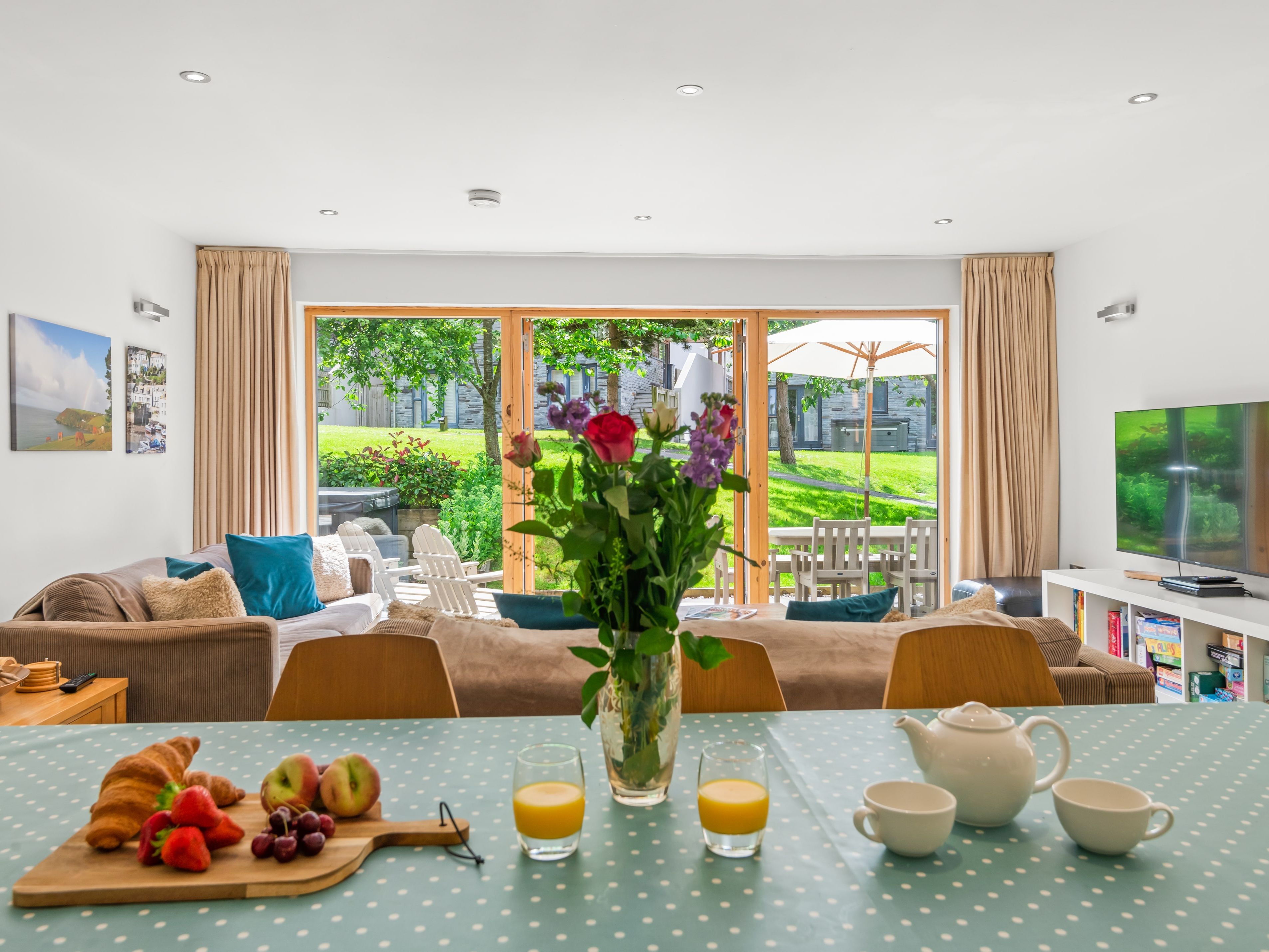 Bright open-plan living and dining room with breakfast table, flowers and garden view through large sliding doors