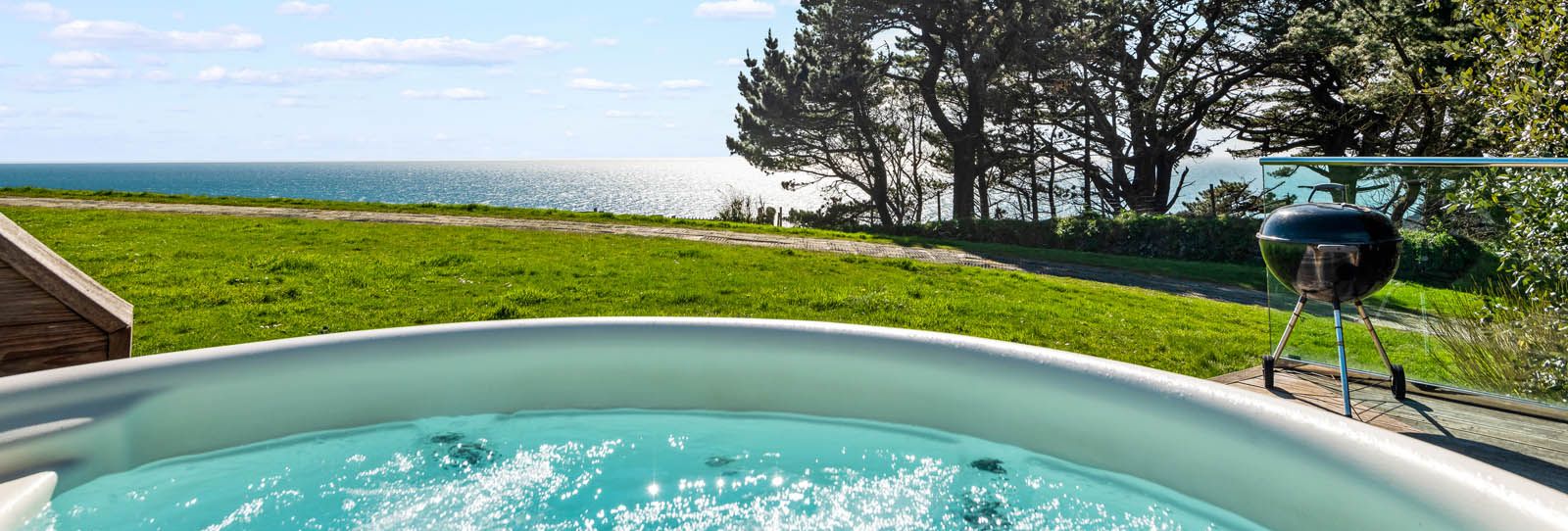 Hot tub on a patio overlooking the sea with trees and a barbecue