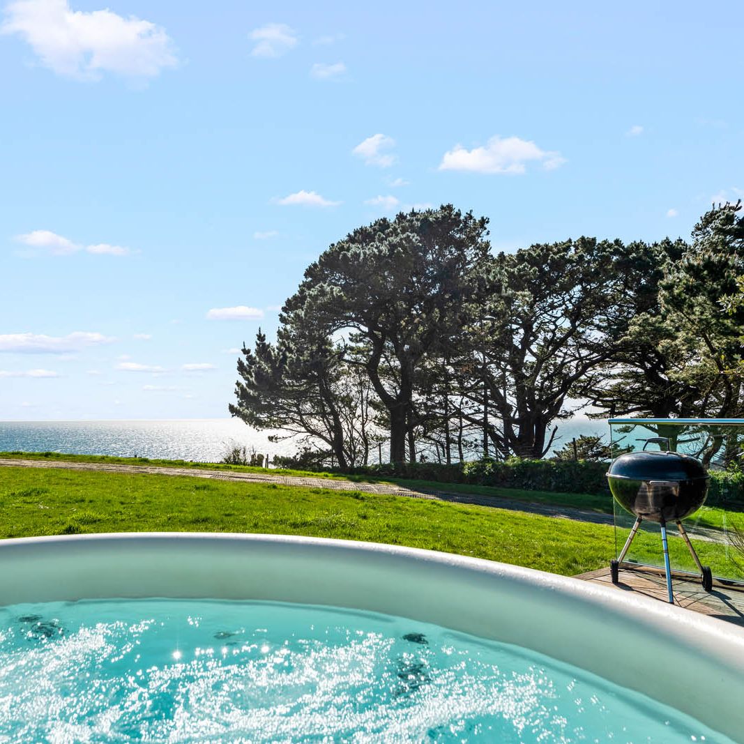 Hot tub on a patio overlooking the sea with trees and a barbecue