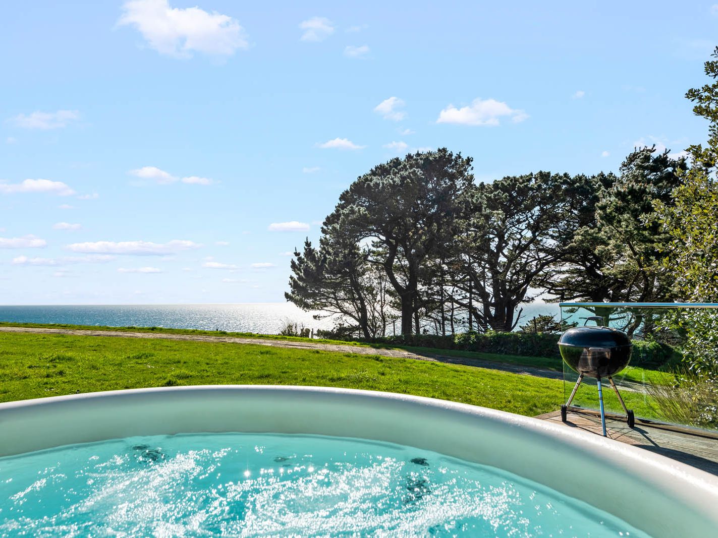 Hot tub on a patio overlooking the sea with trees and a barbecue