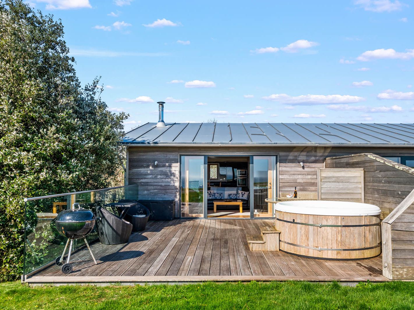 Wooden holiday cabin with deck, hot tub and barbecue on a sunny day