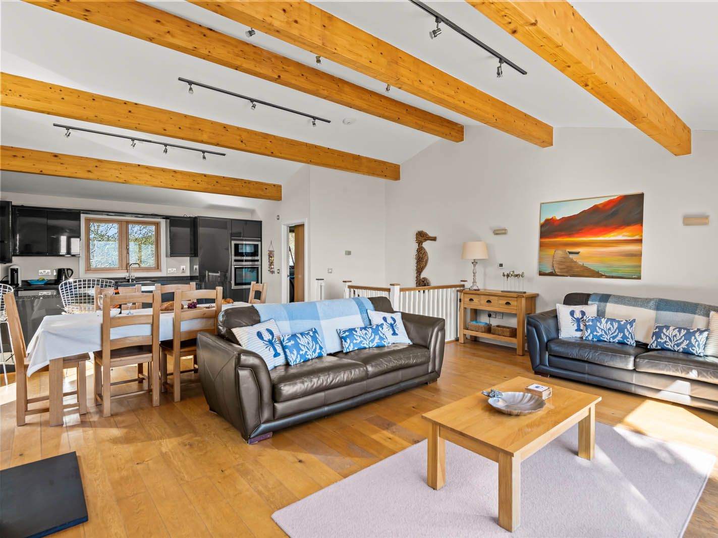 Open-plan living room with exposed wooden beams, leather sofas, dining table and modern kitchen
