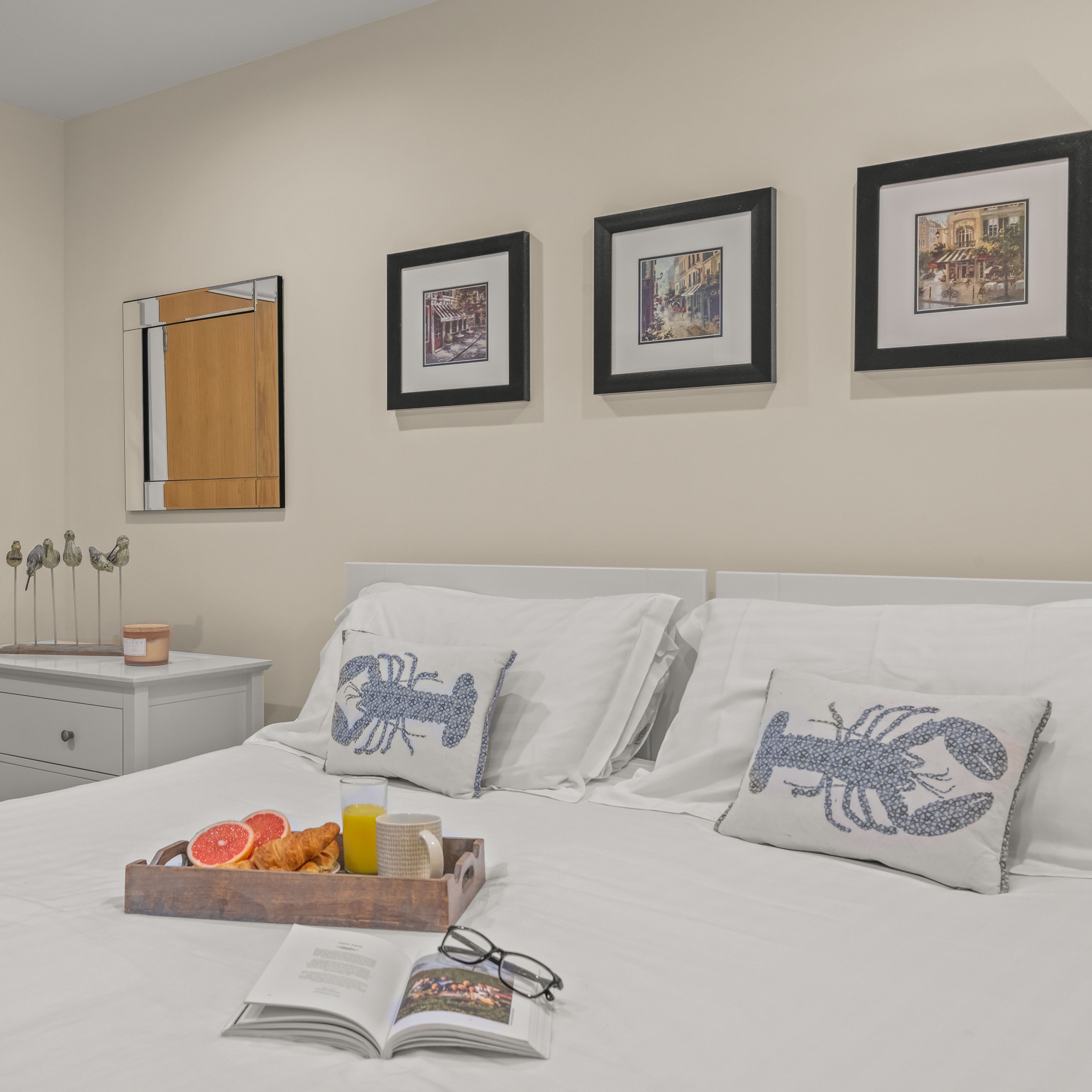 Bright, modern bedroom with white bedding, lobster cushions and a breakfast tray on the bed