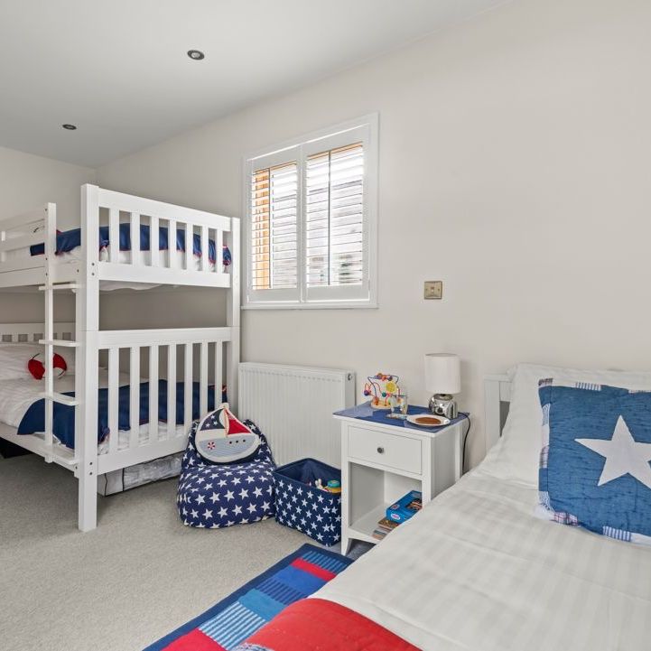 Bright children’s bedroom with white bunk beds, single bed, and navy star-themed cushions and storage.