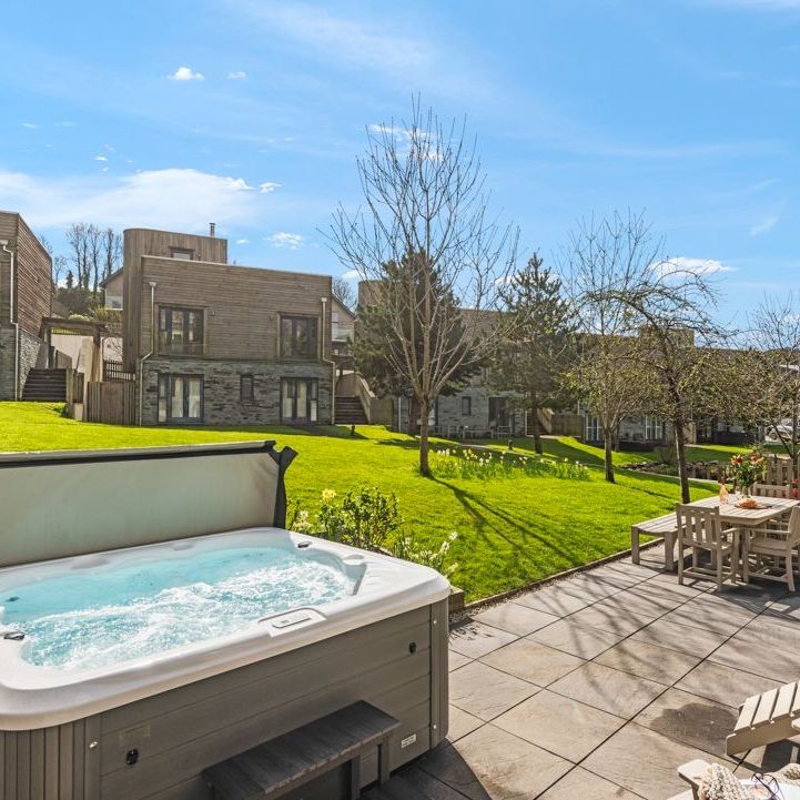 Outdoor hot tub on a sunny patio with garden and modern lodges in the background