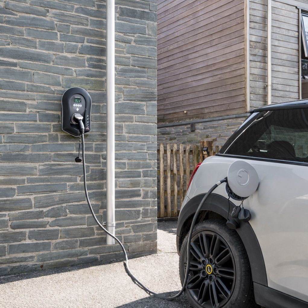 Electric car charging at a wall-mounted home charger beside a stone wall