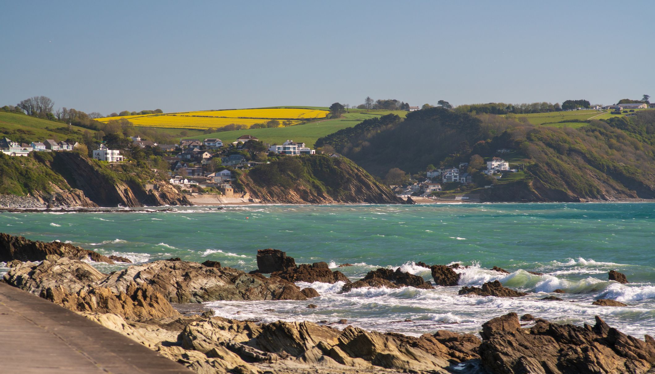 Rocky coastline with turquoise sea and hillside village overlooking yellow and green fields