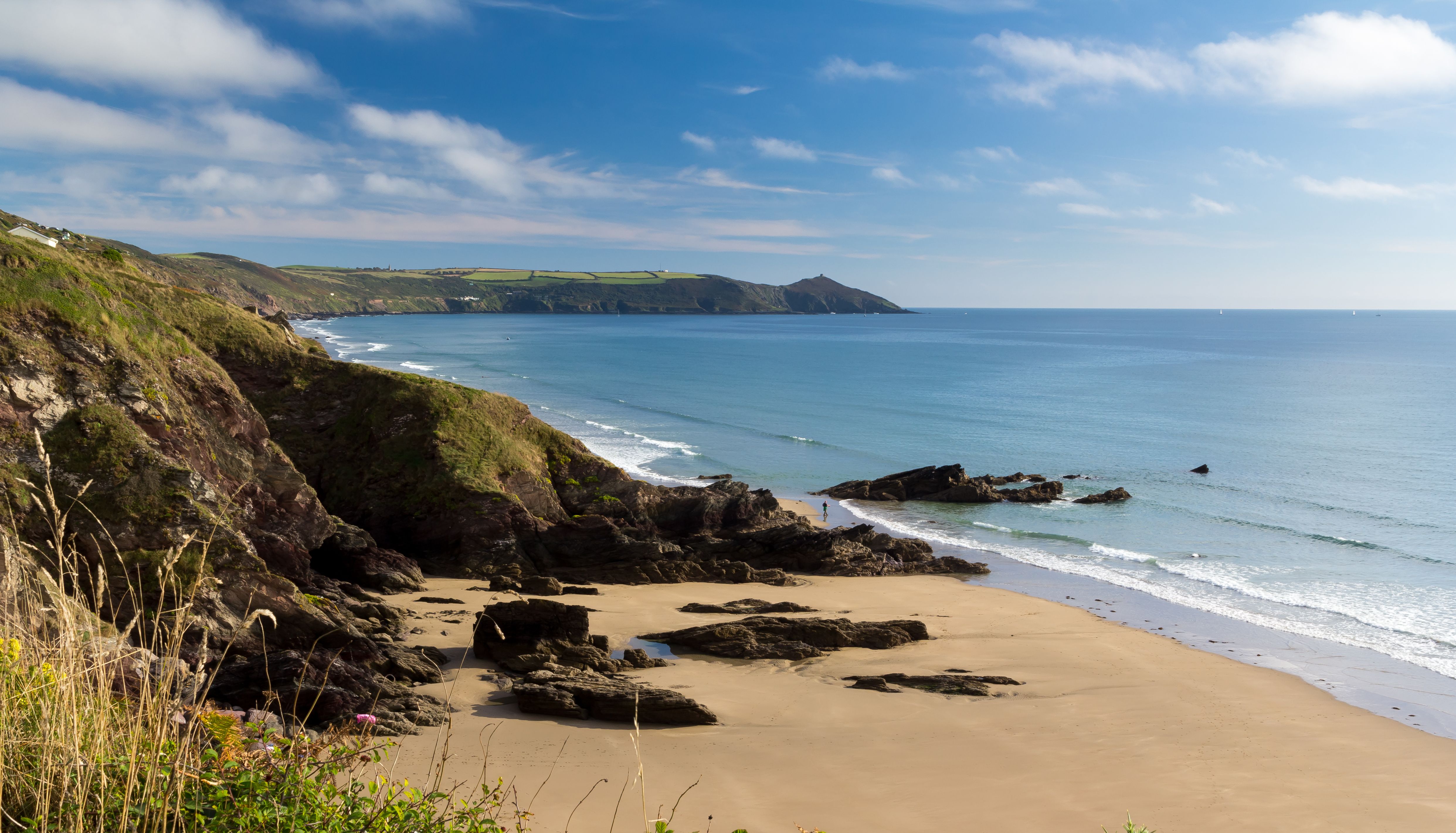 Rocky coastal cove with sandy beach and calm sea under blue sky