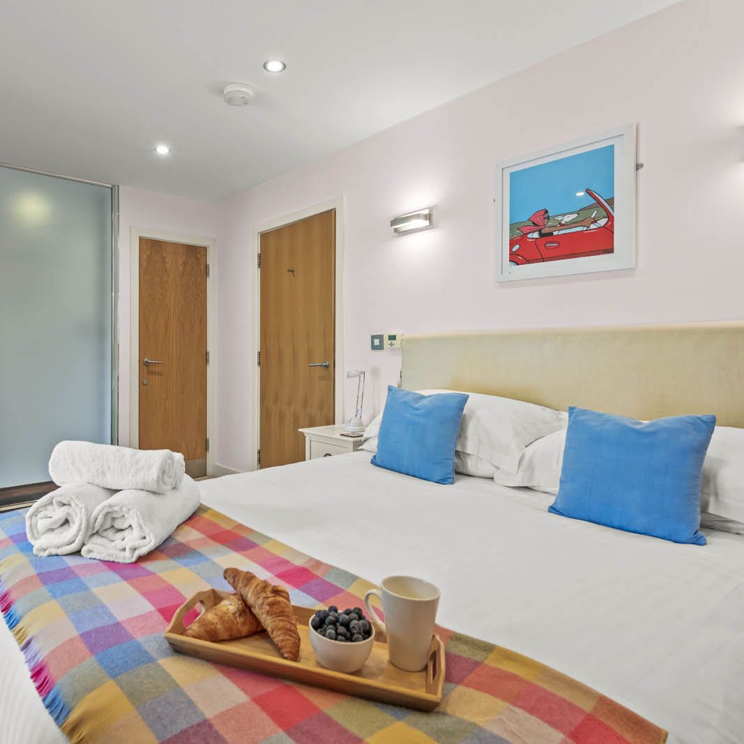 Bright modern bedroom with double bed, blue cushions and breakfast tray, next to an en-suite behind a frosted glass partition