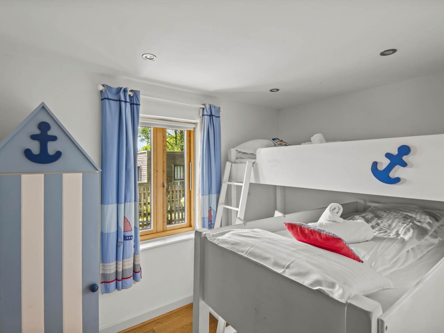 Nautical-themed bedroom with white bunk beds, blue anchor details, and blue curtains by a window