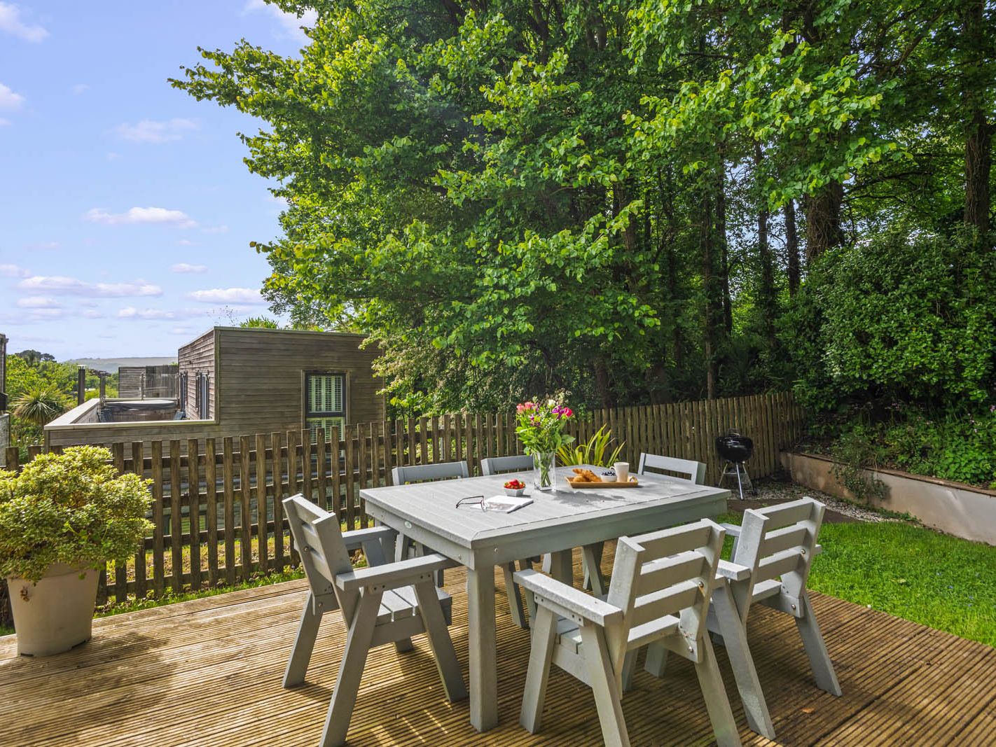 Outdoor dining table and chairs on a wooden deck in a leafy garden