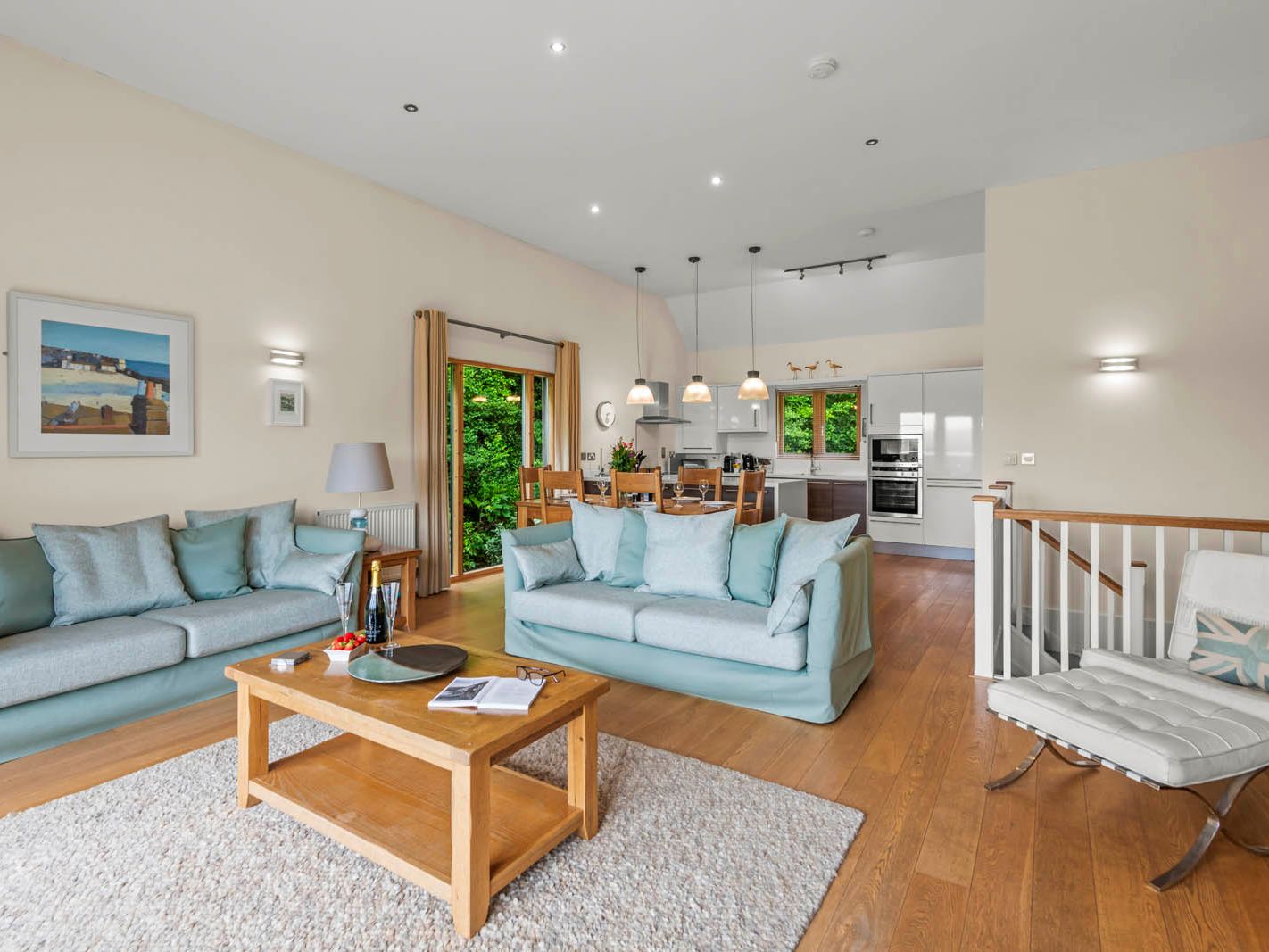 Bright open-plan living room with pale blue sofas, wooden coffee table and modern kitchen with dining area