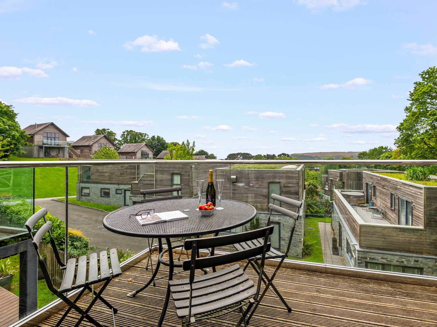 Balcony terrace with round table and chairs overlooking modern wooden lodges and green countryside
