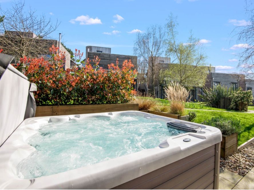 Outdoor hot tub bubbling on a patio beside a landscaped garden and modern houses