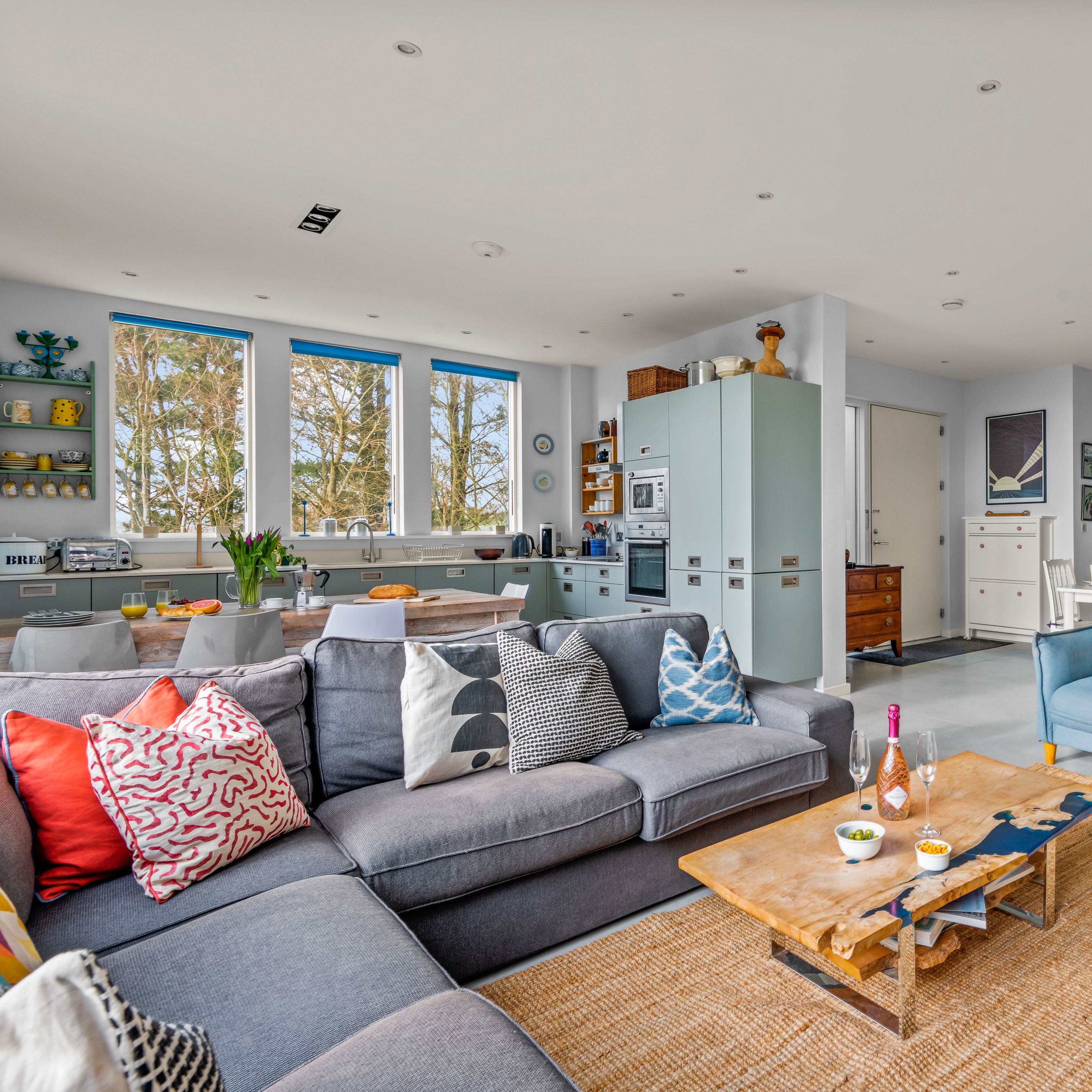 Bright open-plan living room and kitchen with colourful sofas, large windows and a wooden coffee table